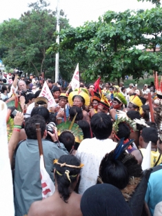 Chief Raoni of the Kayapó people speaks to the crowd, holding his ground in front of a wall of uniformed police
